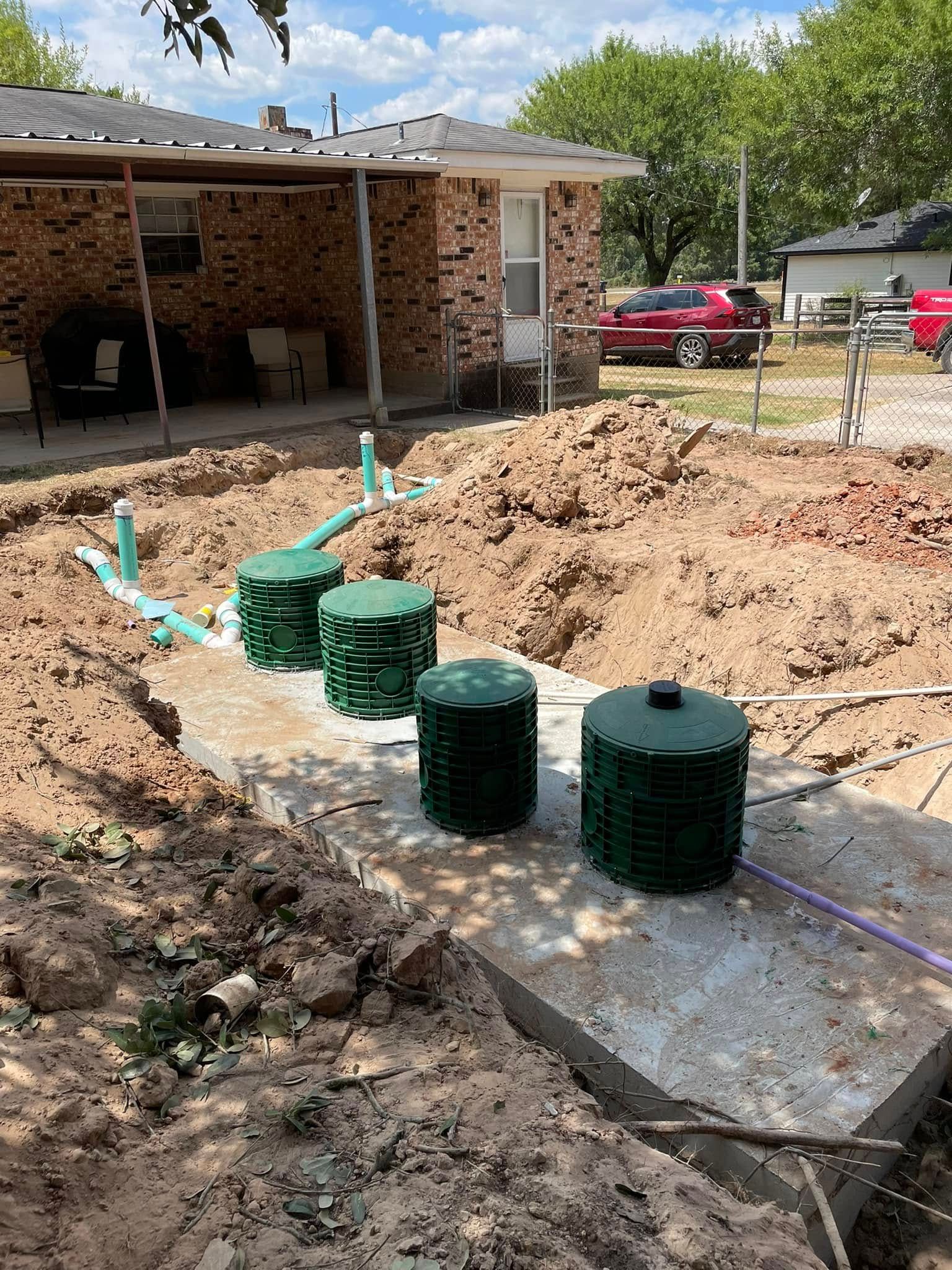 Construction site with three green septic tanks beside a concrete foundation and dirt excavation.