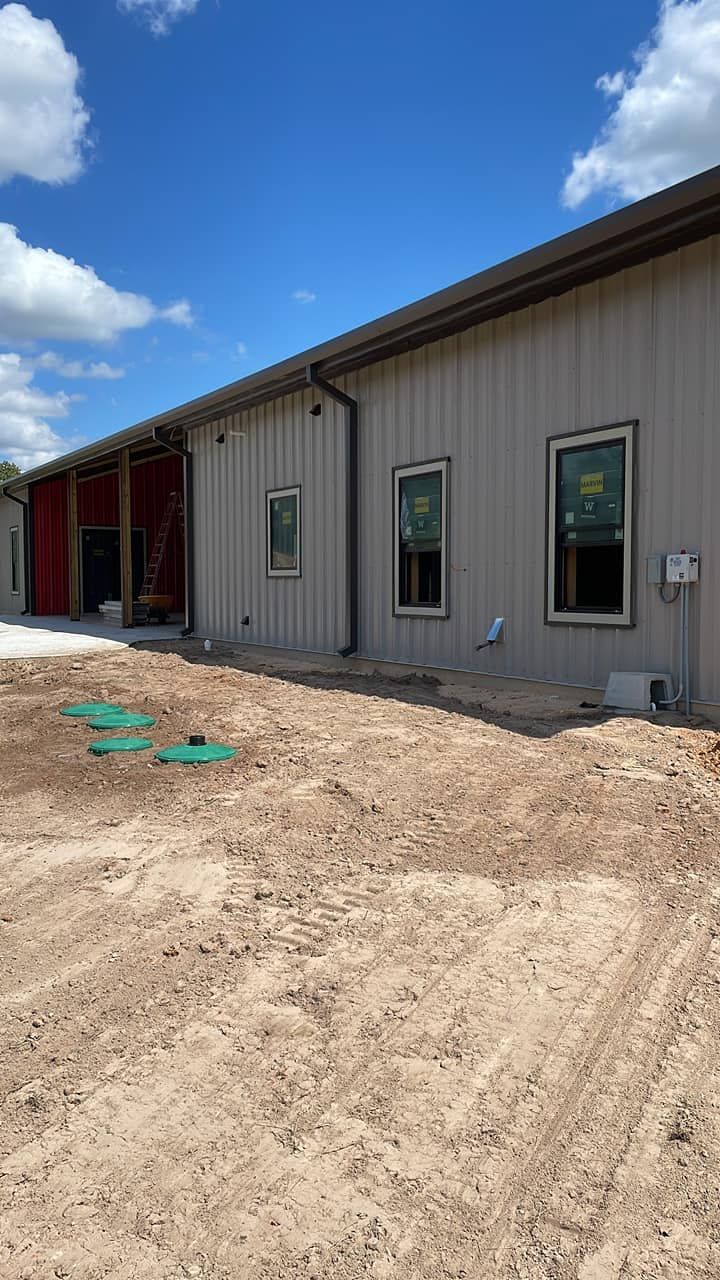 Exterior of a new metal building under construction, with dirt foreground and blue sky.