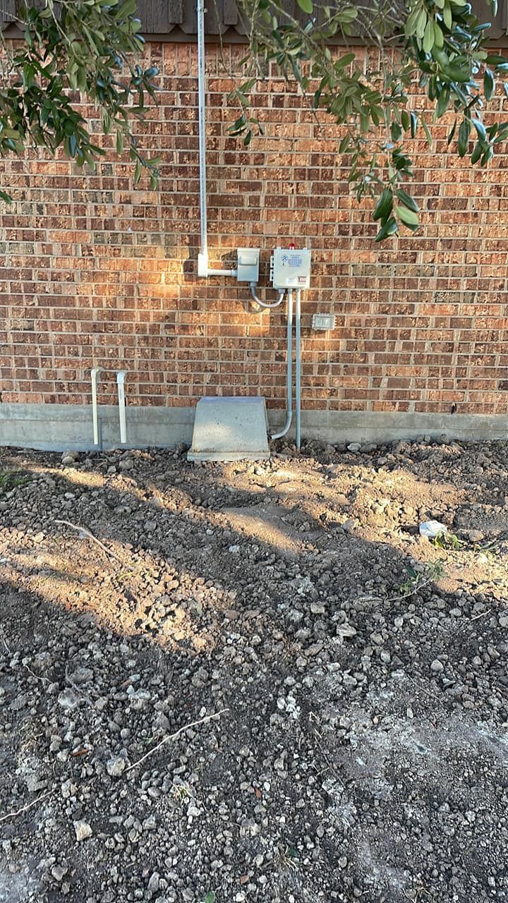Brick wall with utility boxes and gravel ground in front, with hanging greenery above.