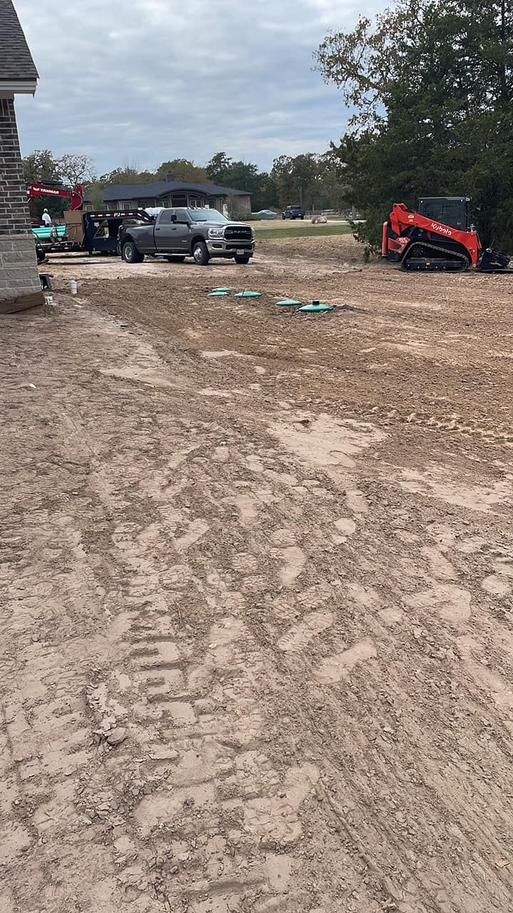 Muddy construction site with a black SUV and a red skid steer on a dirt road under cloudy sky