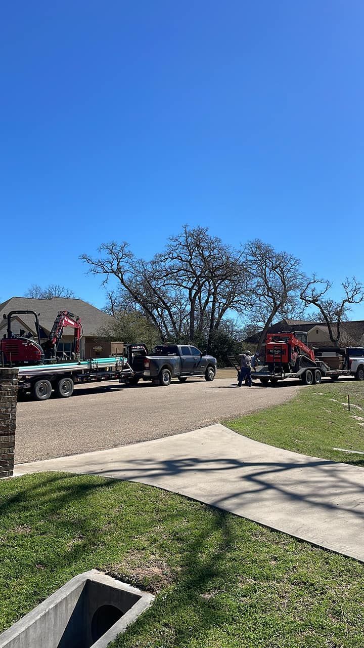 Flatbed tow trucks lined along a roadside under a clear blue sky near a sidewalk and grassy verge