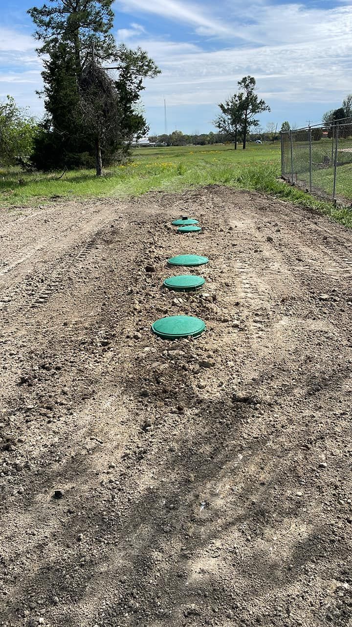Garden path with green circular covers set in a dirt row beside a wire fence under a cloudy sky