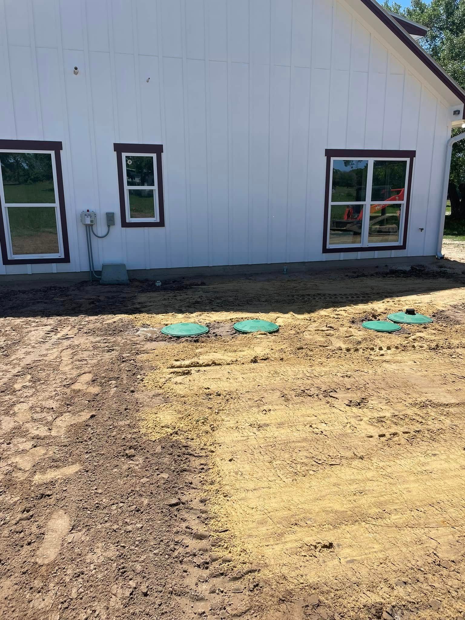 Bare dirt lot in front of a white building with windows and outdoor utility fixtures.