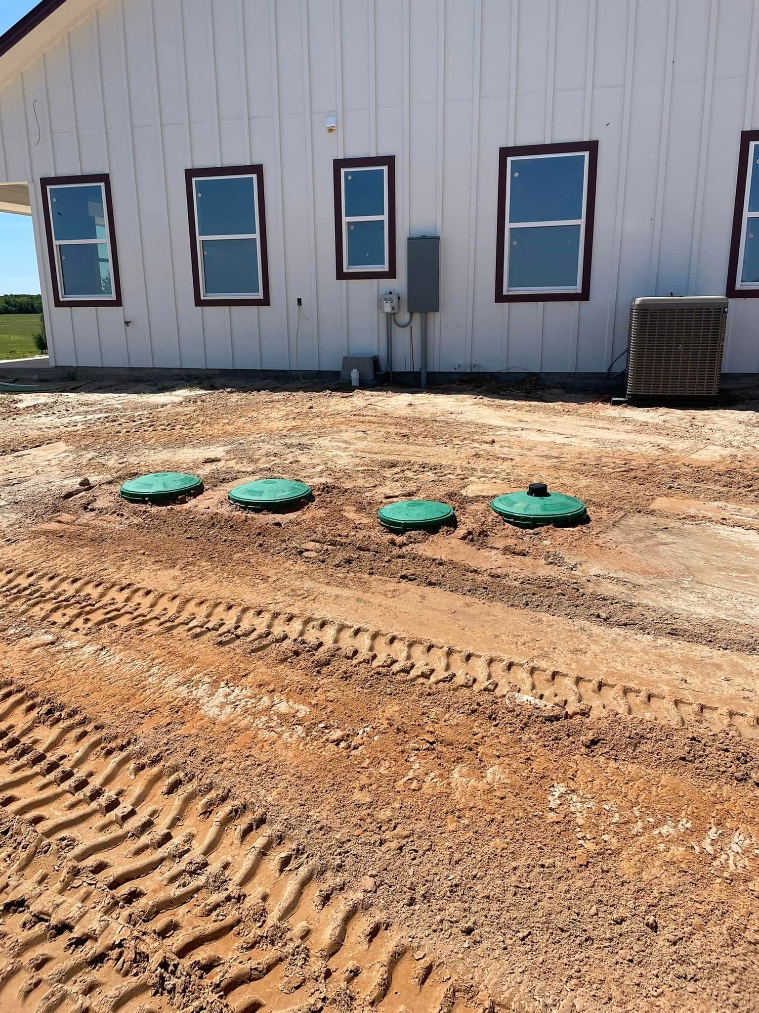 Gravel construction site beside a white building with windows and green utility covers in the foreground