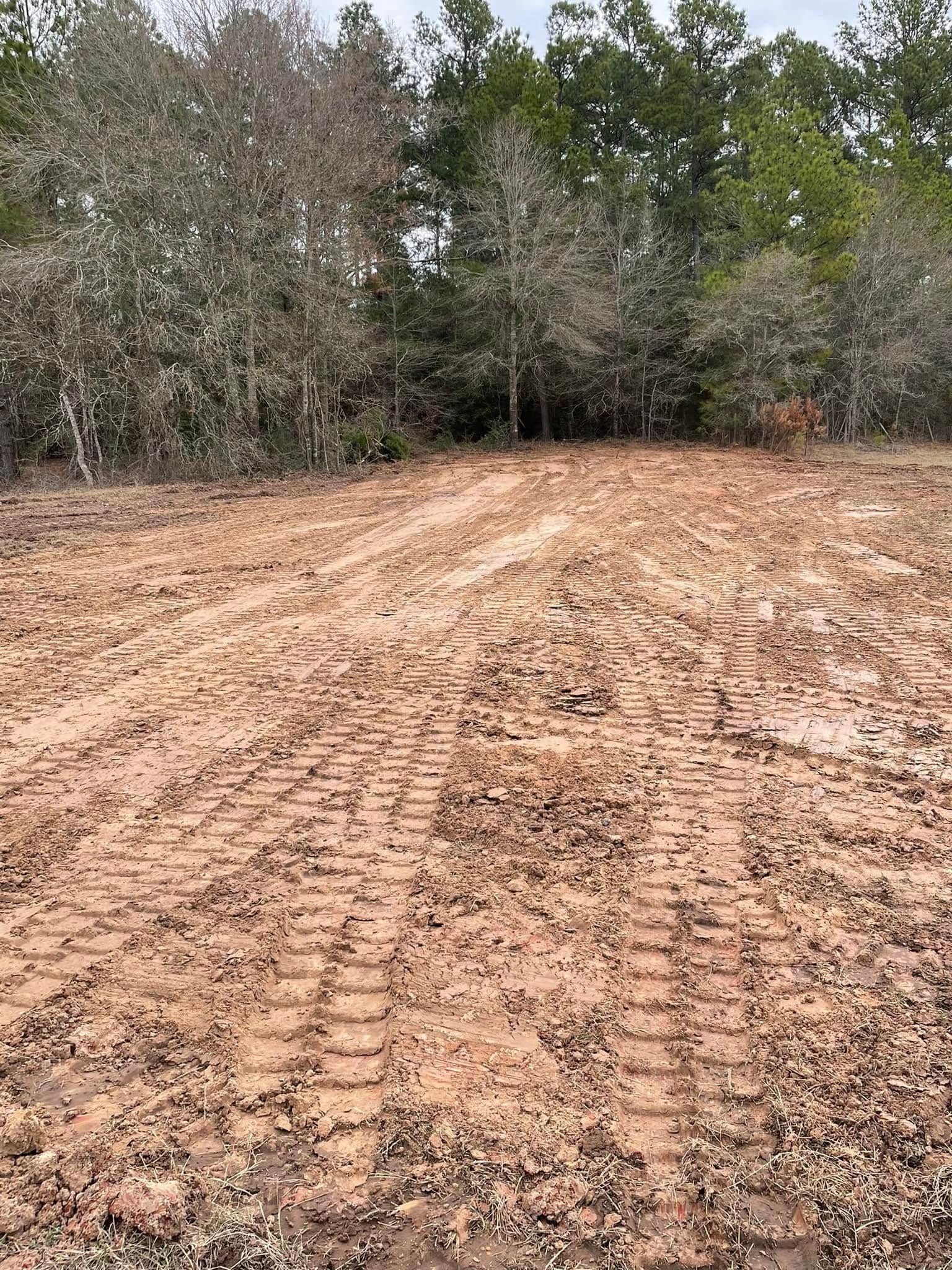 Mud-covered dirt clearing with tire tracks, bordered by dense trees and brush.