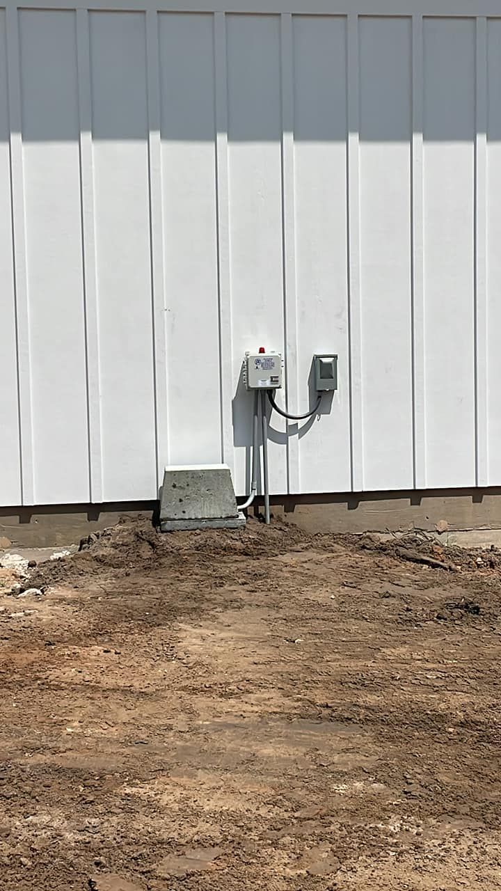 White exterior wall with utility meters and conduit above bare dirt ground