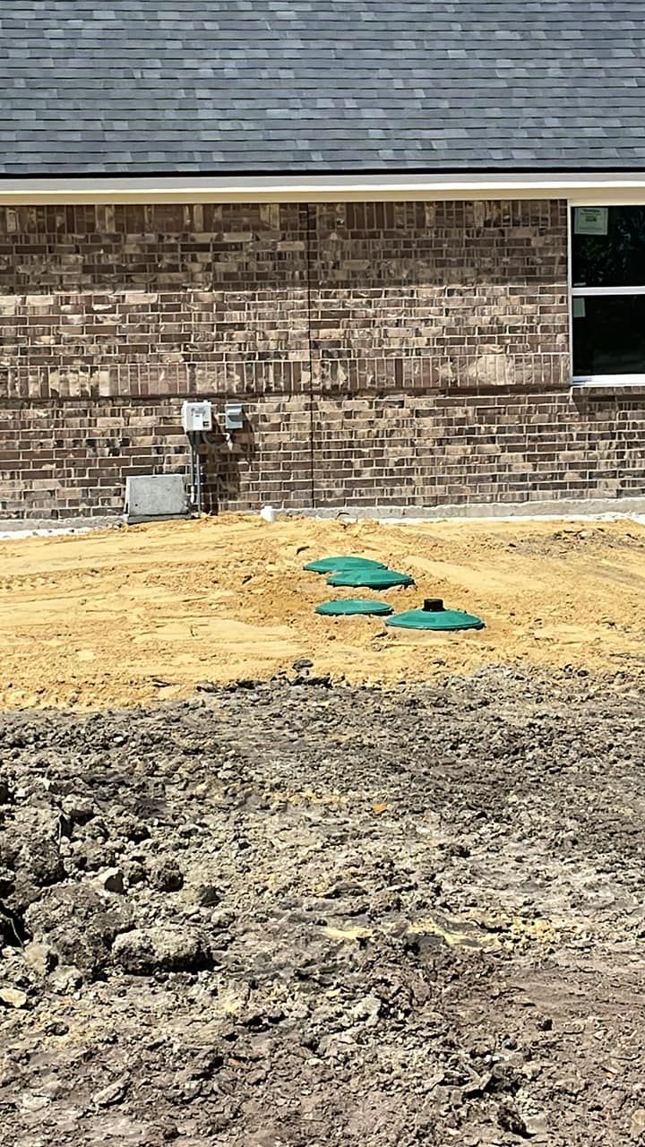 Backyard under construction with dirt, a brick house wall, and teal covered utility lines.