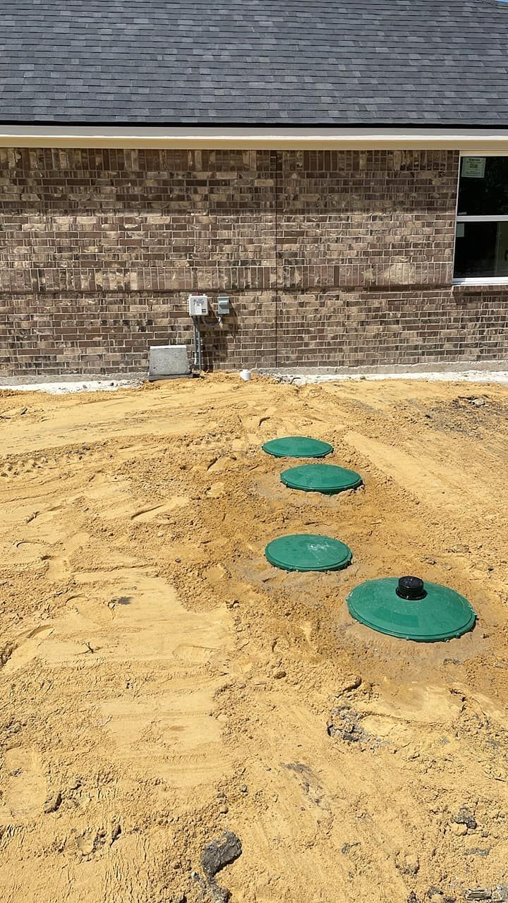 Construction site with four green utility caps in a dirt area beside a brick building.