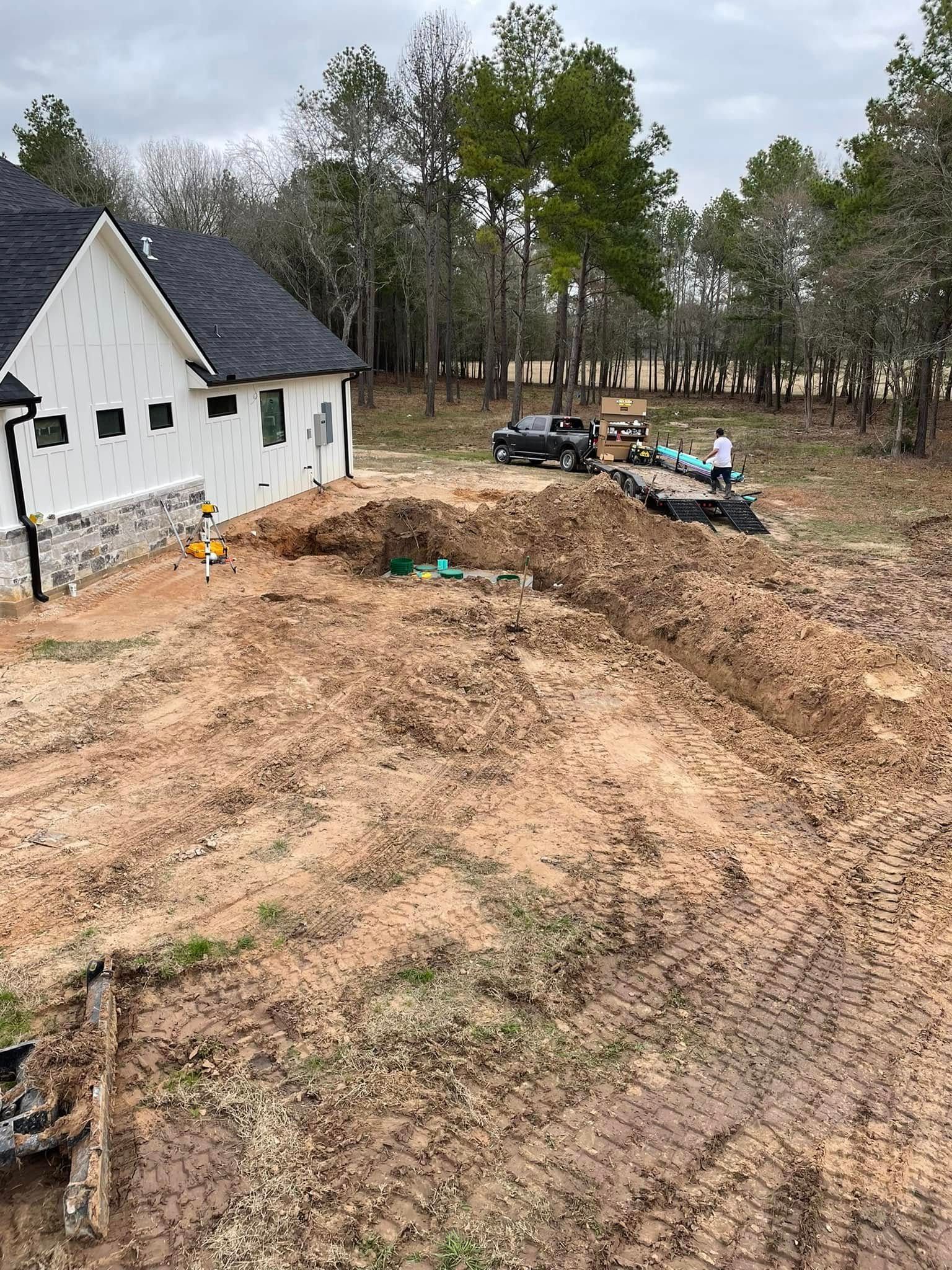 New house under construction with muddy dirt piles, a parked truck, and trees in the background
