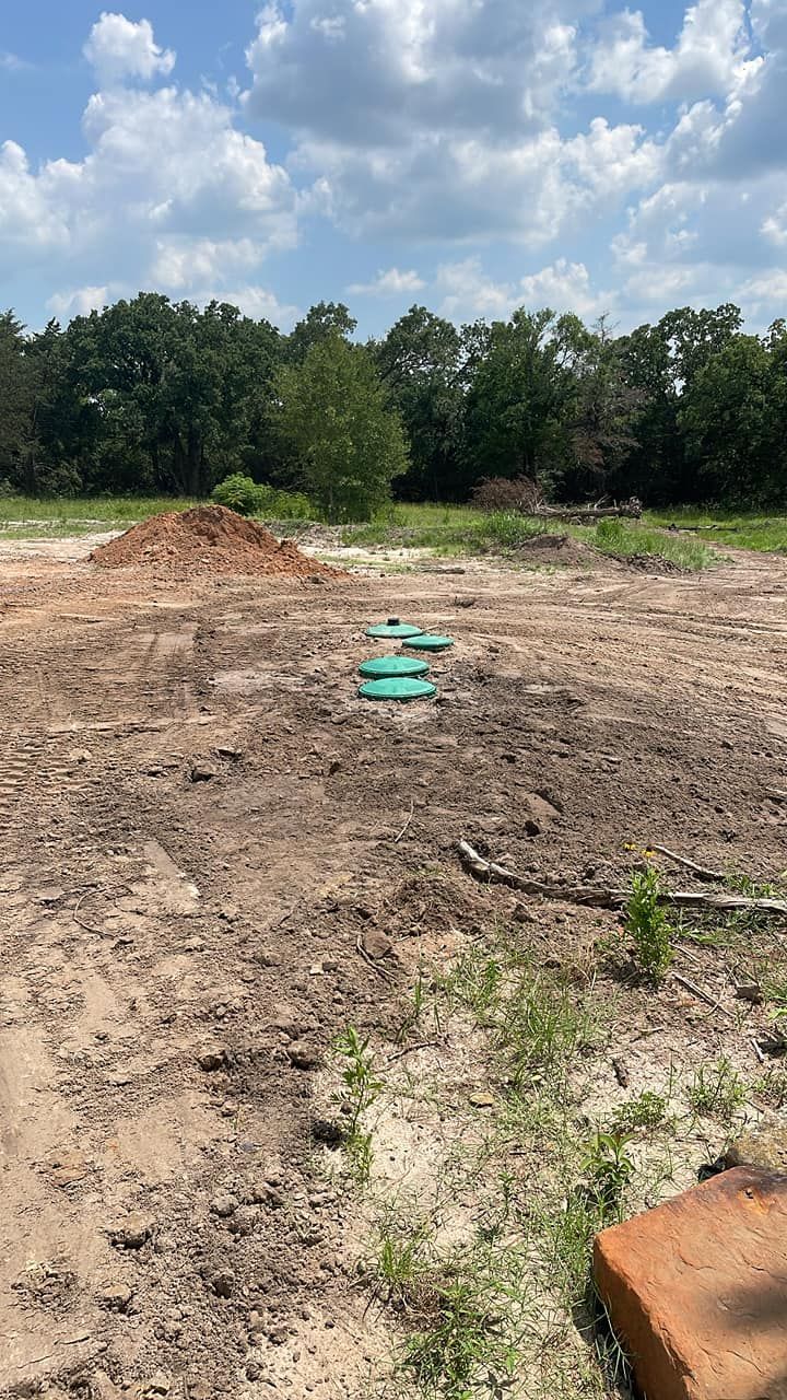 Cleared dirt lot with a small green pipe in the center and trees under a cloudy sky