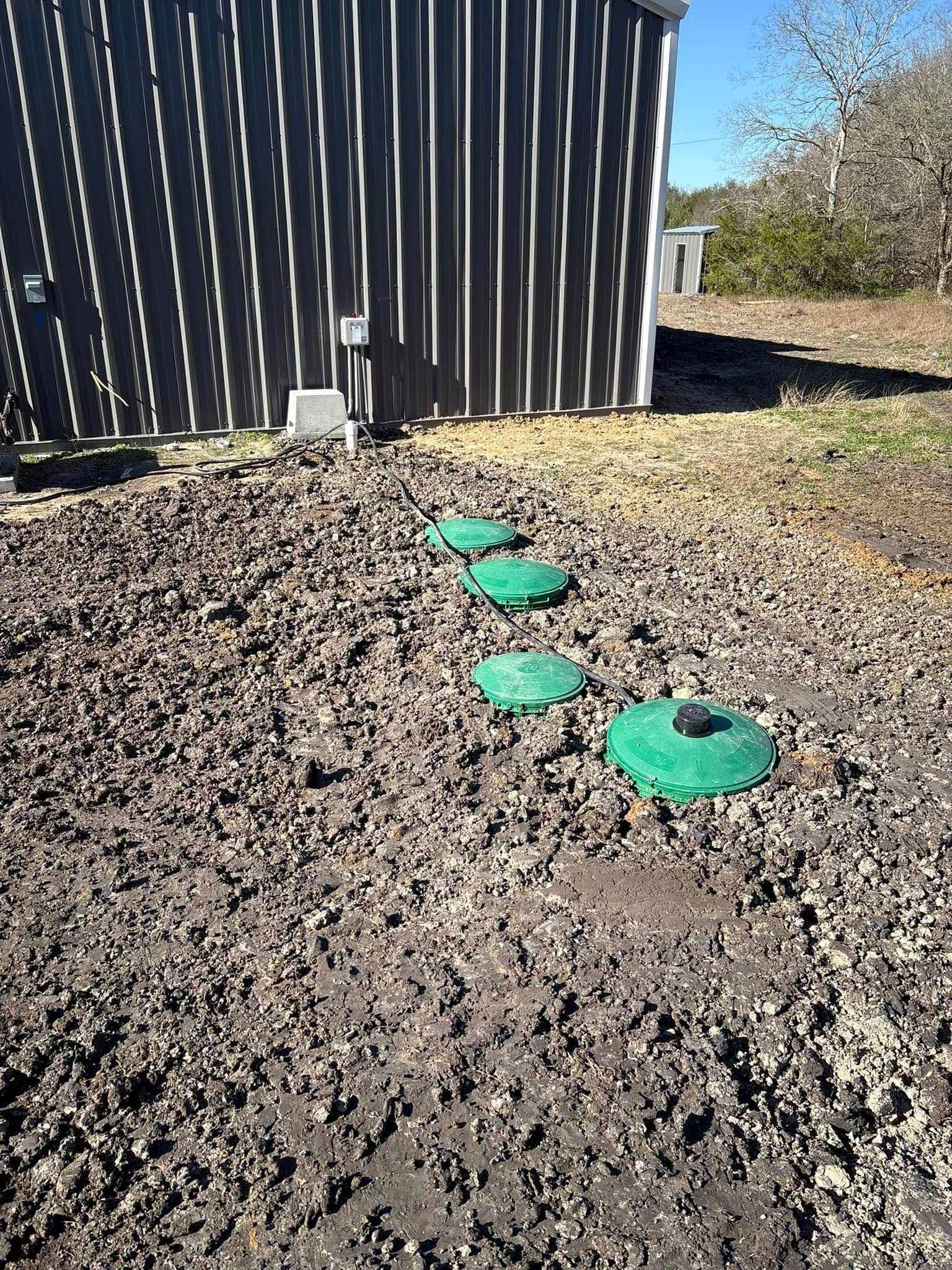 Three green circular lids in a dirt yard beside a dark corrugated building