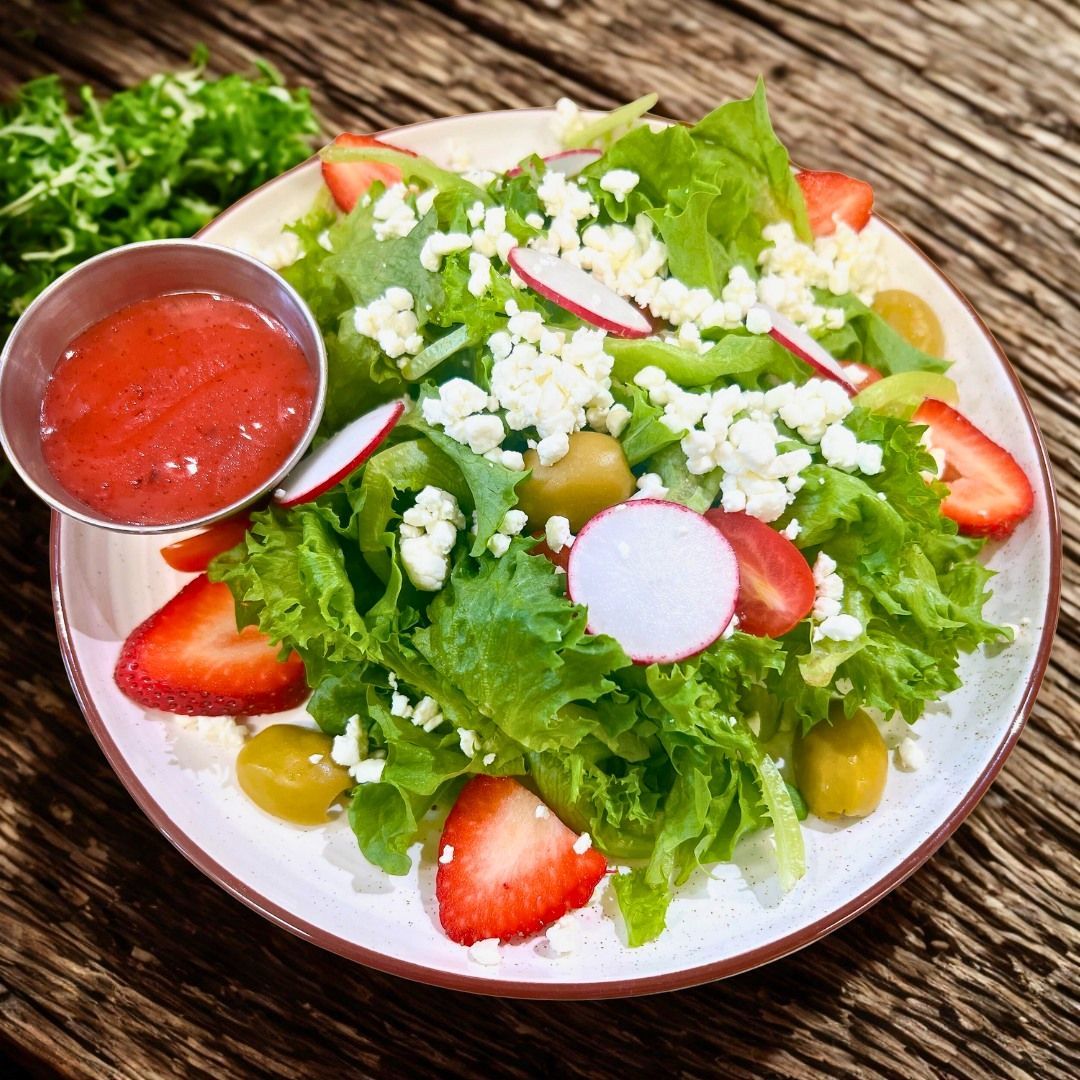 Salad with strawberries, olives, radishes, and feta cheese with a side of red dressing.