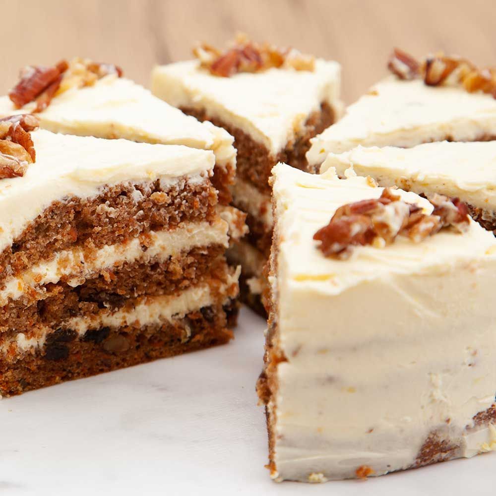 Carrot cake slices with white frosting and pecans on a marble surface.