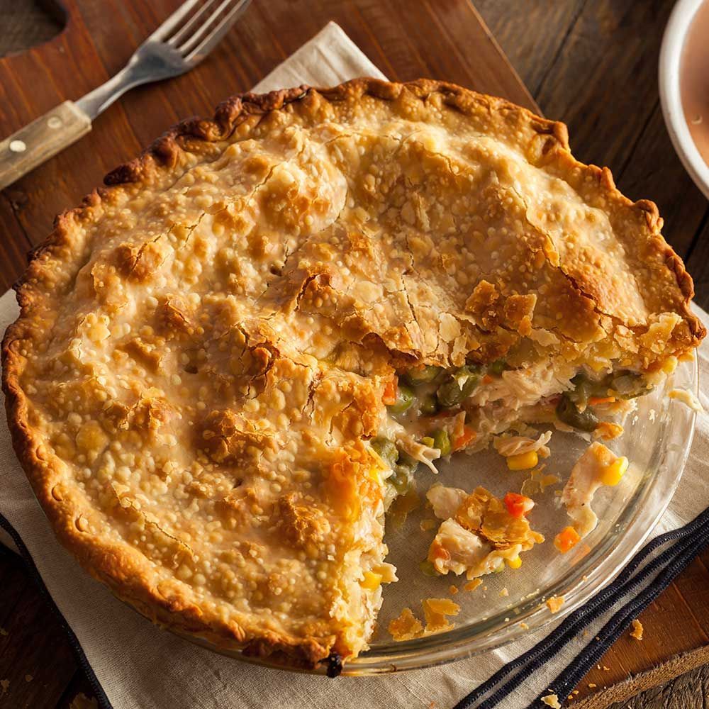Chicken pot pie with golden crust, cut to reveal chicken and vegetables inside.