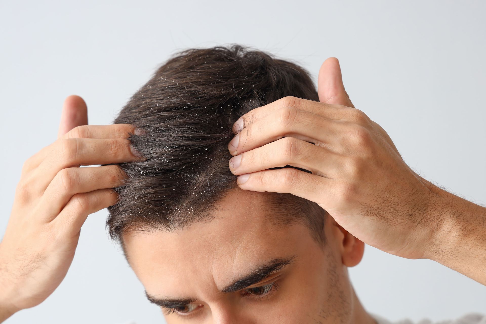 Pessoa penteando o cabelo escuro para trás com as duas mãos contra um fundo branco.