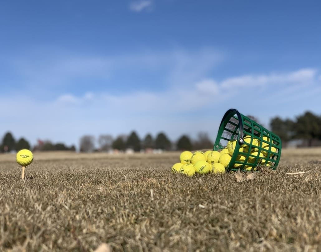 A green basket filled with golf balls is sitting on top of a dry grass field.