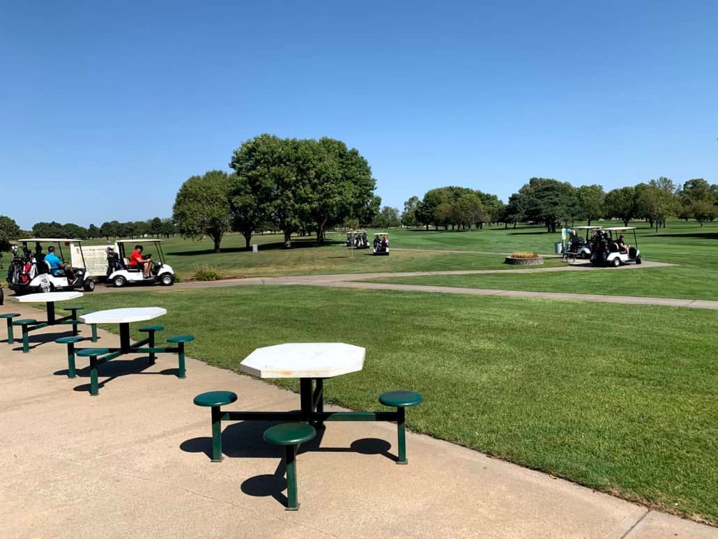 A group of golf carts are parked on the side of a golf course.