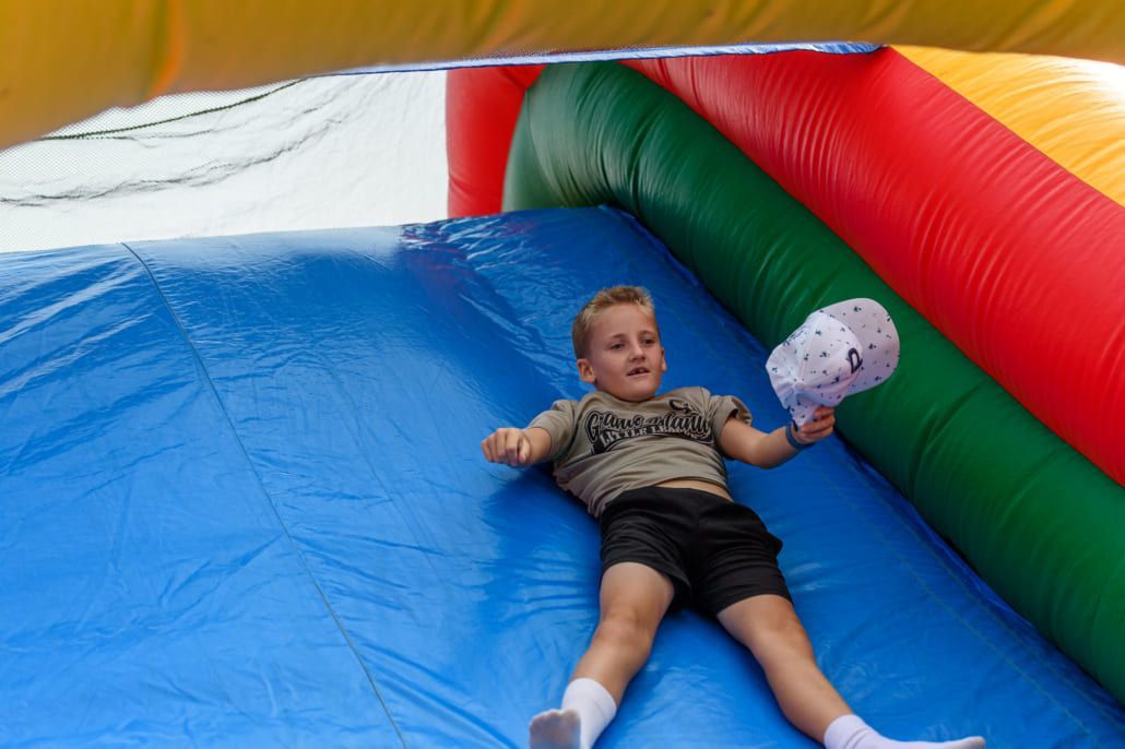 A young boy is laying on top of an inflatable slide holding a cotton candy.