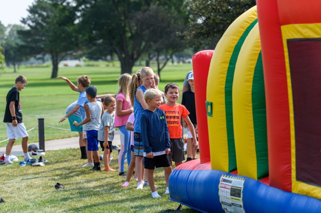 A group of children are standing in front of a bouncy house in a park.