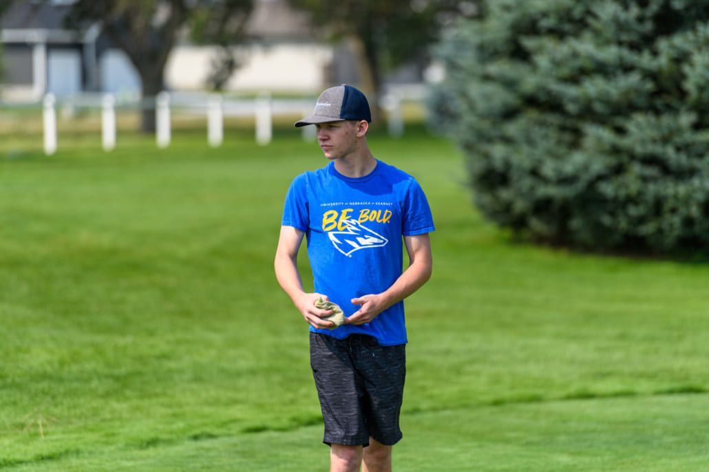 A man in a blue shirt and black shorts is standing in a grassy field holding a frisbee.