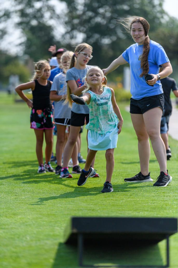 A group of children are playing a game of cornhole on a lush green field.