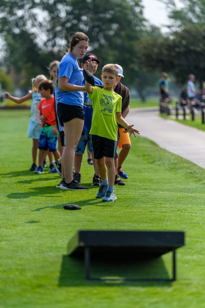A group of children are playing a game of cornhole in a park.