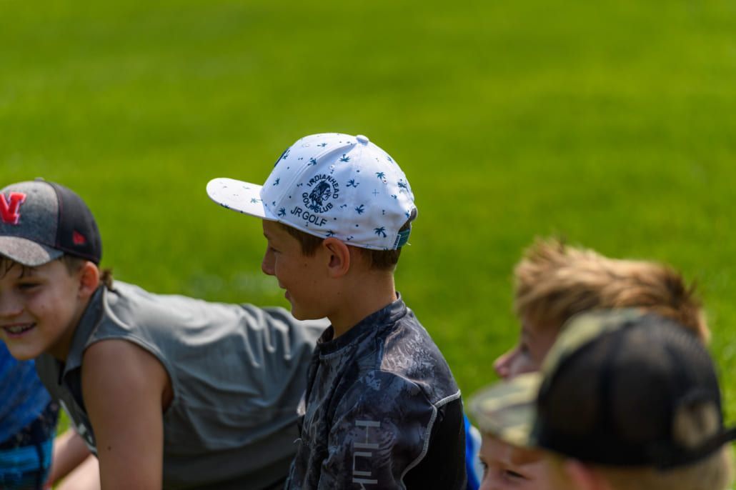 A group of young boys wearing baseball caps are sitting on the grass.