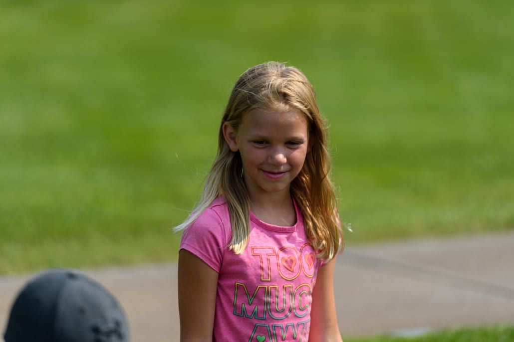 A young girl in a pink shirt is sitting on a sidewalk in a park.
