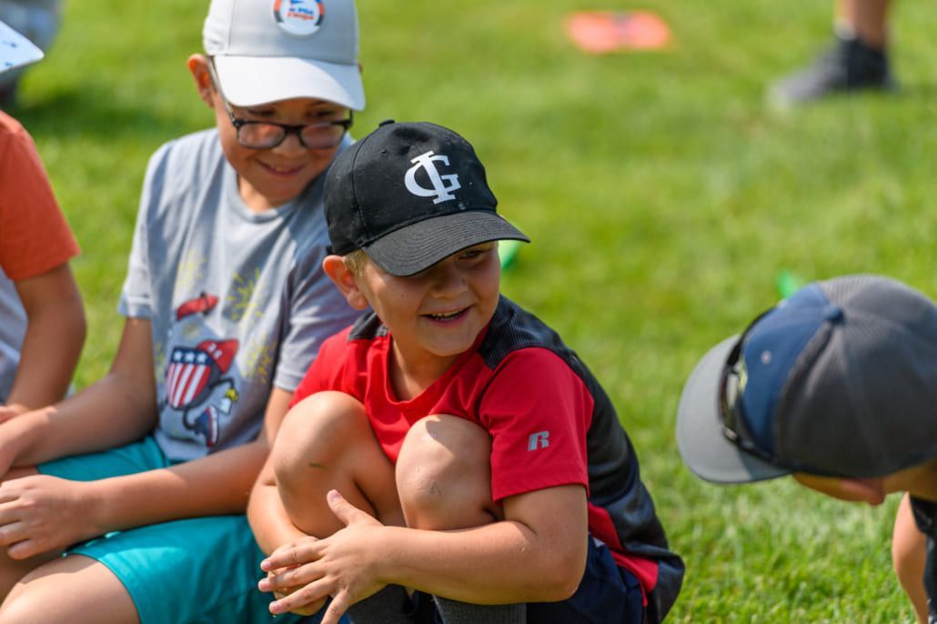 A group of young boys are sitting on the grass wearing baseball caps.