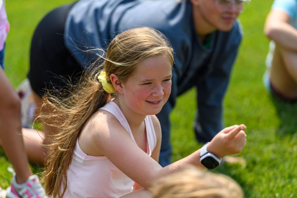 A young girl is sitting in the grass with a watch on her wrist.