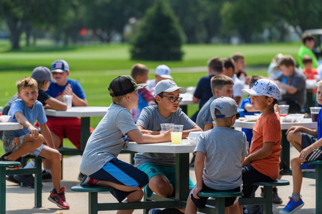 A group of young boys are sitting at picnic tables in a park.