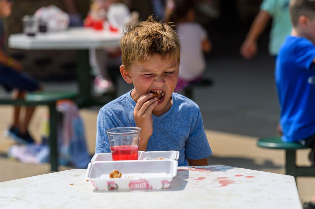 A young boy is sitting at a table eating a donut and drinking juice.