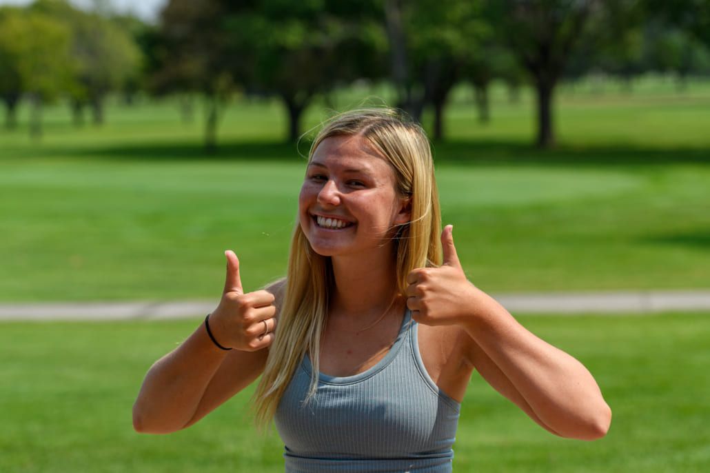 A young woman is giving a thumbs up in a park.