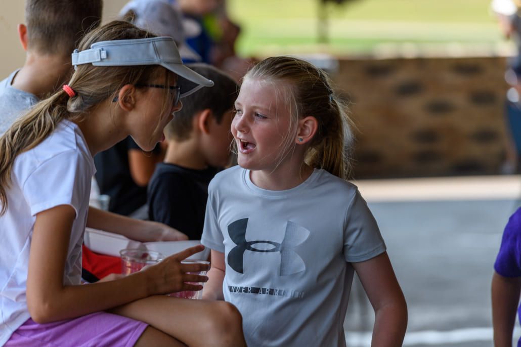 Two young girls are sitting next to each other and talking to each other.