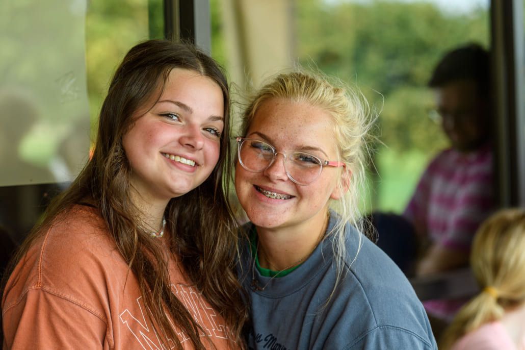 Two young women are sitting next to each other and smiling for the camera.