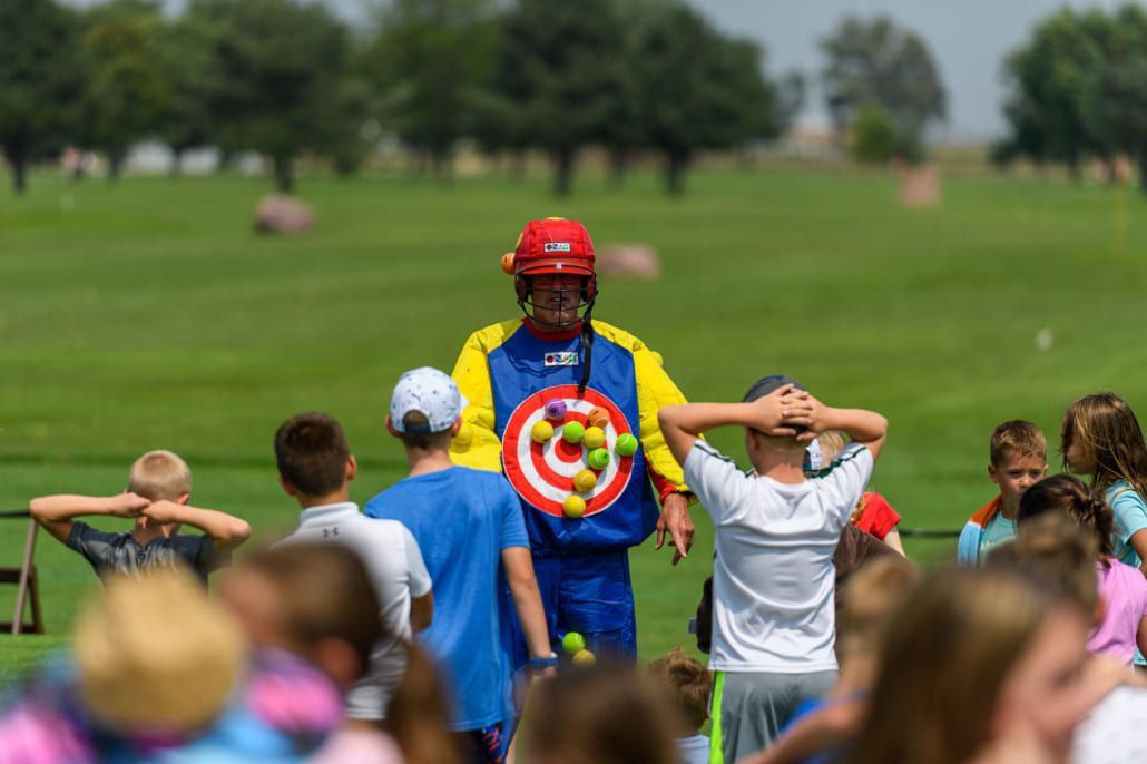 A clown is holding a target in front of a crowd of children.