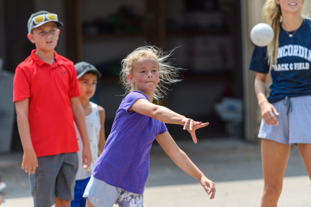 A girl in a purple shirt is throwing a ball.
