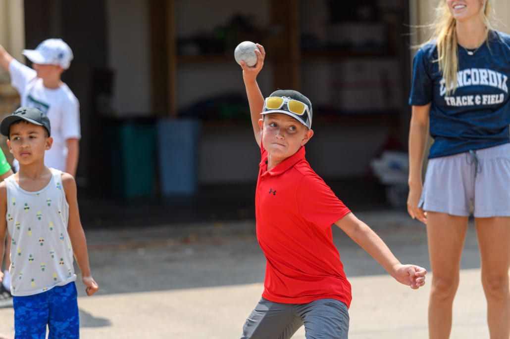 A young boy throwing a baseball wear a red shirt.