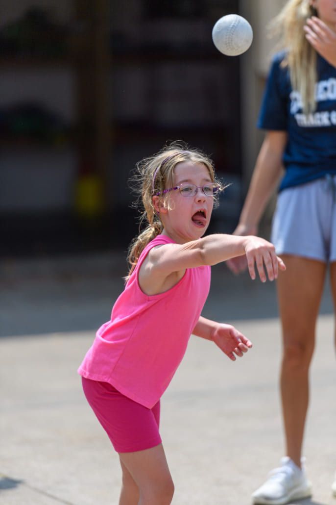 A little girl in a pink tank top is throwing a ball.