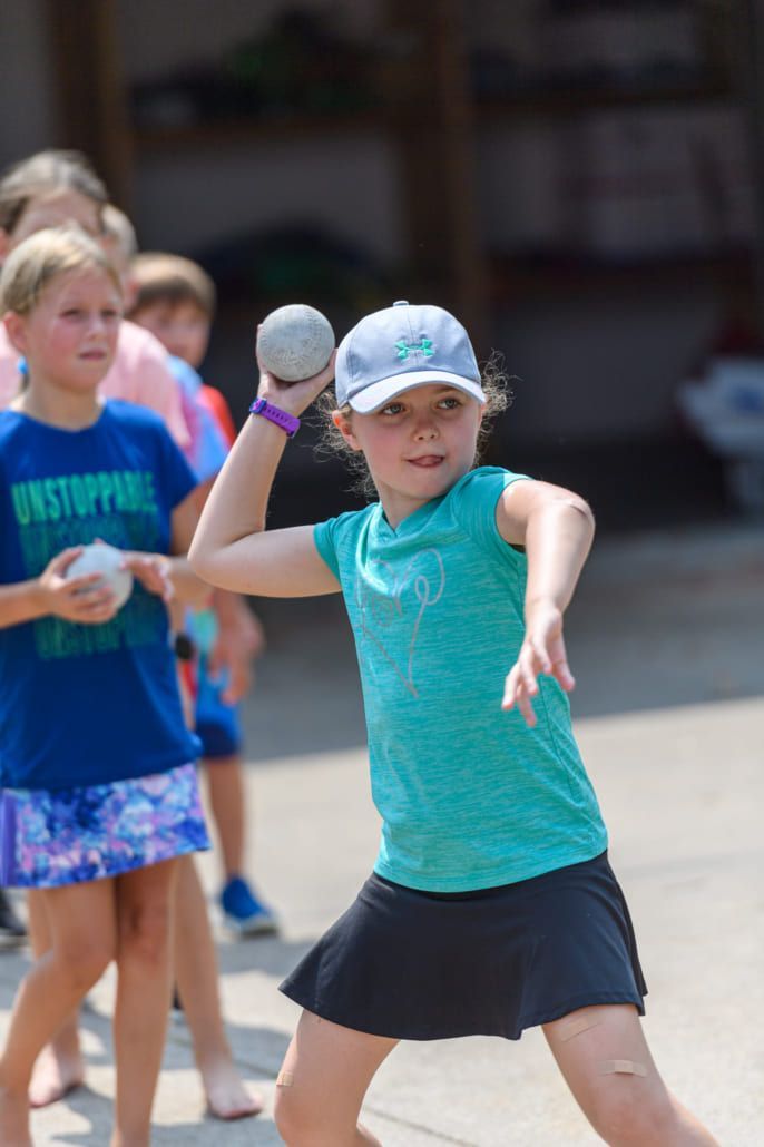 A girl wearing a blue shirt that says evertoppine is throwing a ball