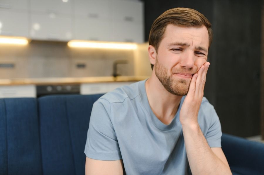 A man is sitting on a couch with a toothache.