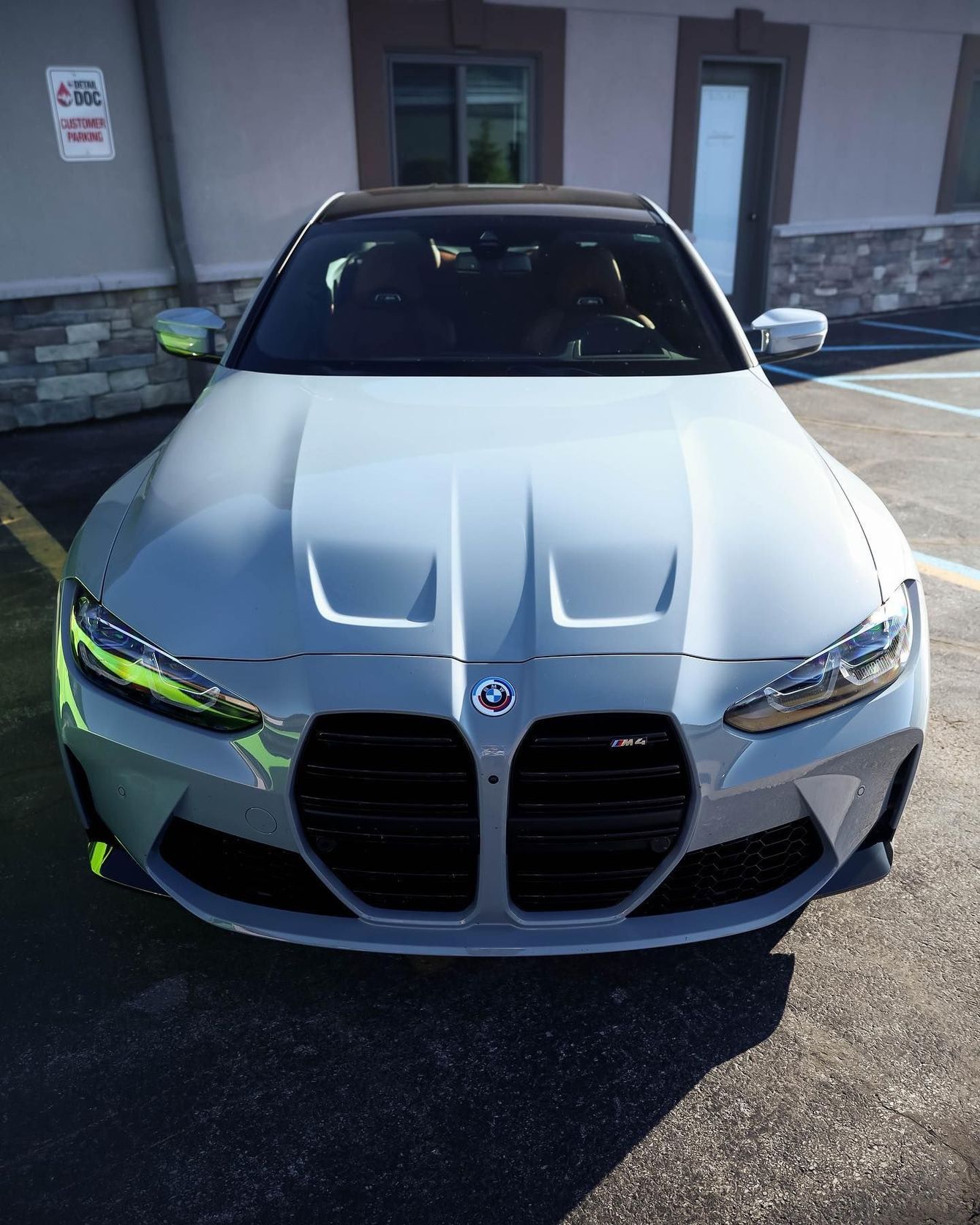 a white bmw m4 is parked in a parking lot in front of a building .