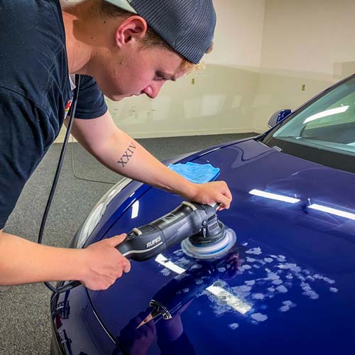 A man is polishing a blue car with a machine.