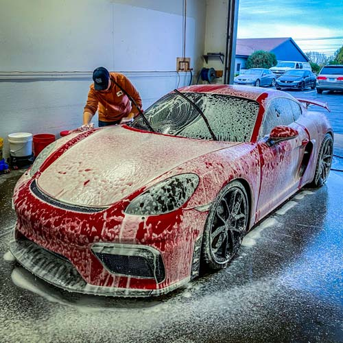 A man is washing a red sports car with foam in a garage.
