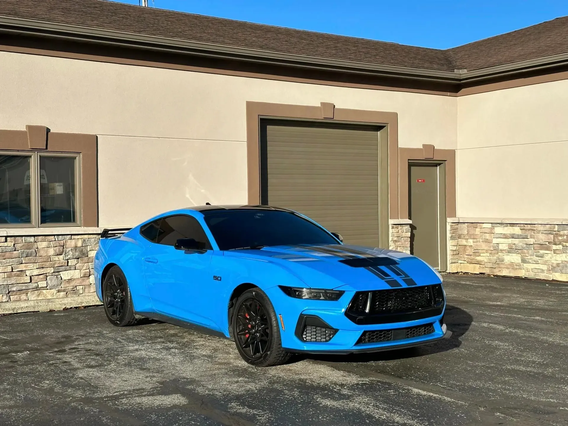 A blue mustang is parked in front of a building.