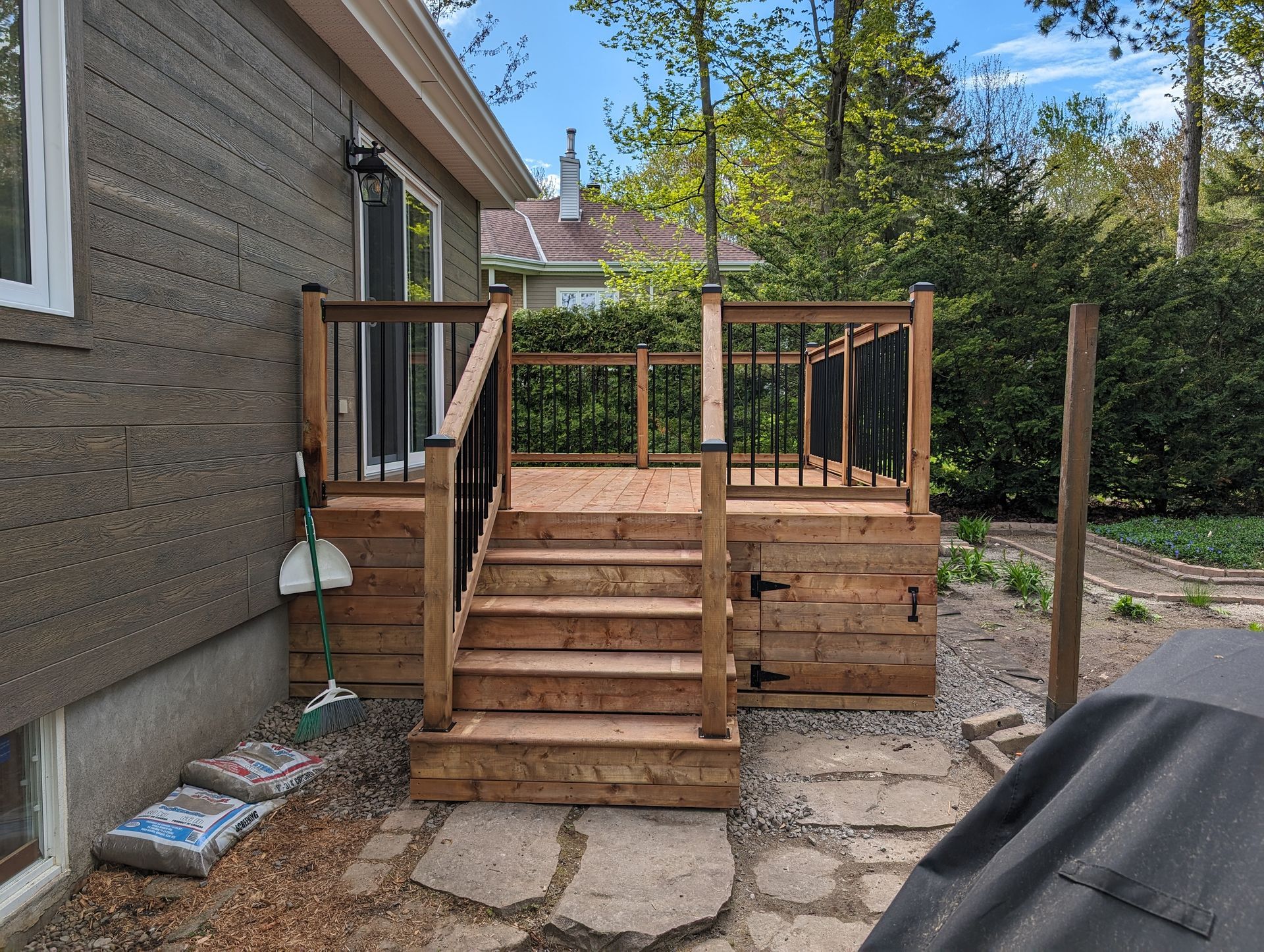 Terrasse en bois avec escalier menant à une plate-forme surélevée; balustrade, chemin en pierre et extérieur de la maison.
