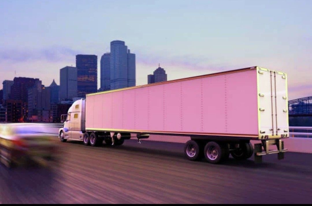 White semi-truck hauling a pink trailer on a city highway at dusk