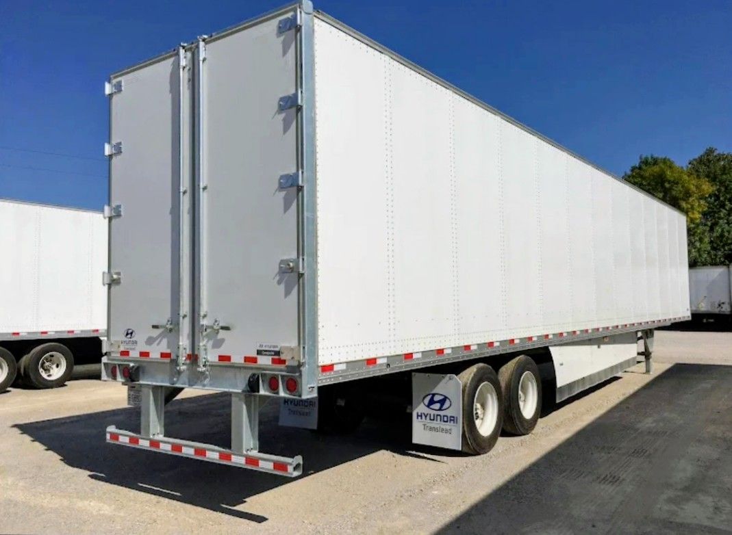 White semi-trailer truck parked outdoors on a sunny lot, viewed from the rear-left side.