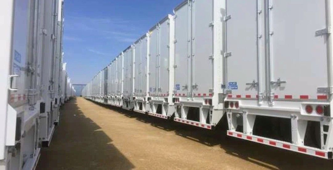 Rows of white semi-trailers lined up on a dirt road under a blue sky