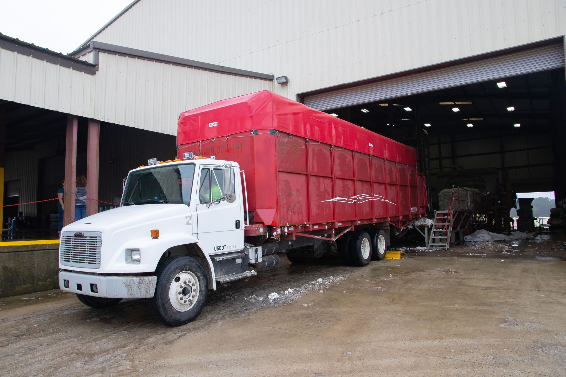 White truck with red covered cargo parked at a warehouse loading bay